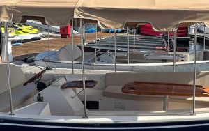 Seaforth Boat Rentals - Blogs 3 Part Of A Boat Deck With Beige Seating And A Canopy, Docked At A Marina With Jet Skis In The Background.