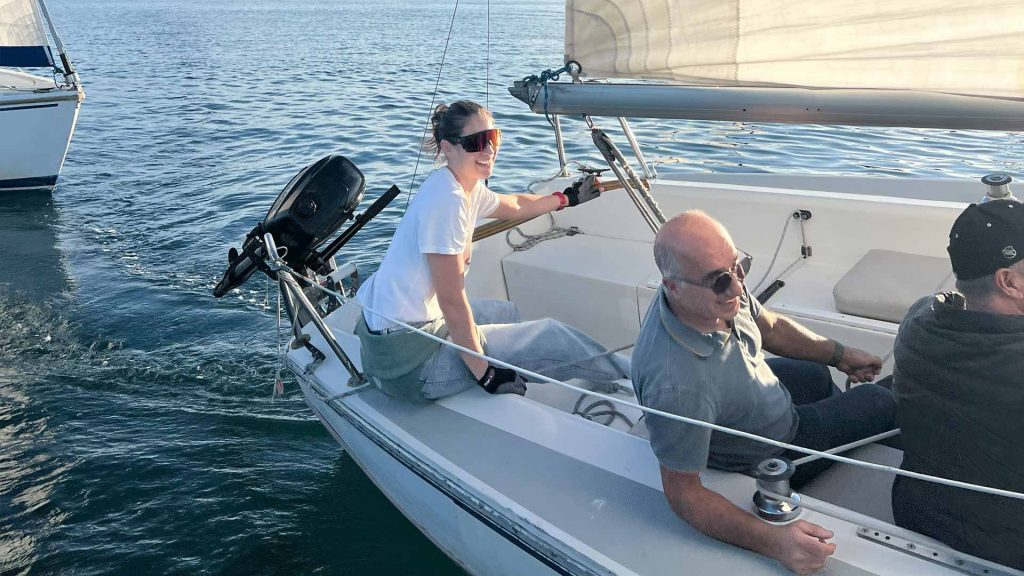 Three people sailing on a calm sea with clear skies.