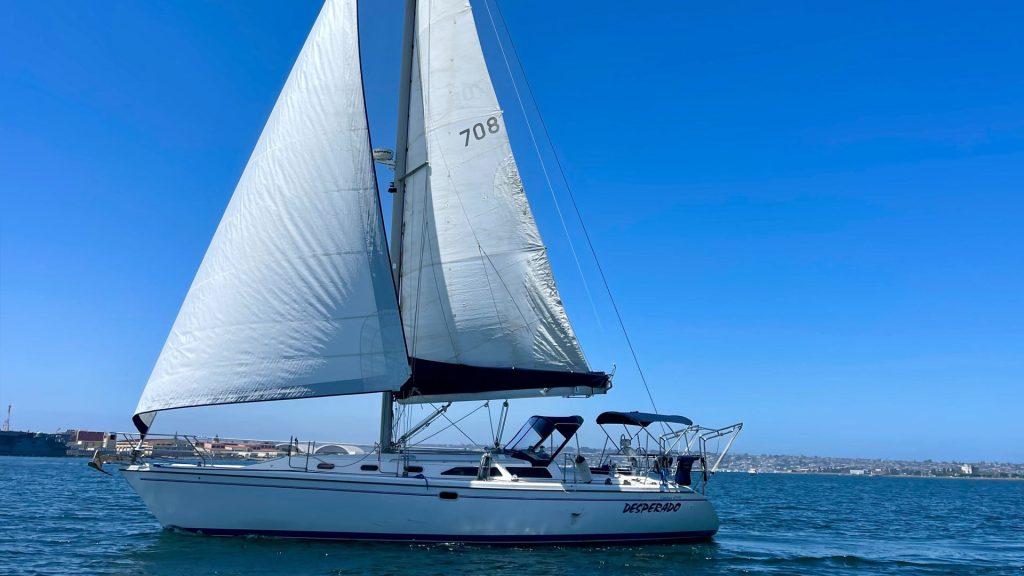 Sailboat with white sails on blue water under clear sky.