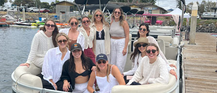 Group of people in white outfits on a boat by a dock.