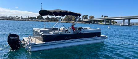 A pontoon boat on calm waters with a bridge in the background.