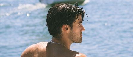 A person with dark hair, seen from behind, gazes at a serene blue water scene on a sunny day.