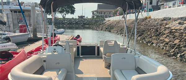 View from the back of a boat, showcasing spacious seating, a calm waterway, and a marina with various boats and people in the distance.