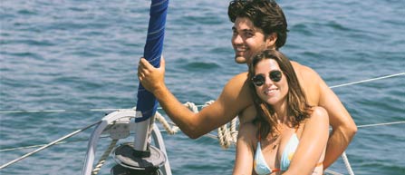 A couple enjoys a sunny day on a sailboat, surrounded by calm water, embracing each other while relaxing together.