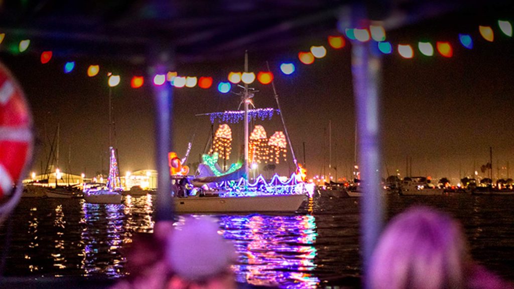Colorfully illuminated boats parade on a calm night waterway, with festive lights reflecting against the surface.