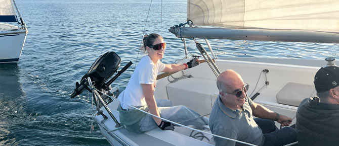 Three people sailing on a calm sea next to another boat.