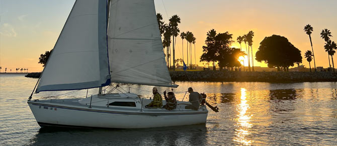 Sailboat with passengers at sunset, near a palm-lined shore.