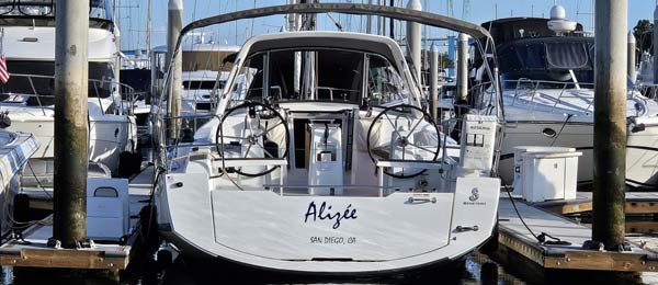 A white sailboat named Alizée docked in a marina with other boats in the background.