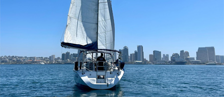 A sailboat with unfurled sails on blue water with a clear sky.