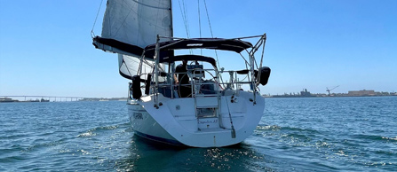 A sailboat with unfurled sails on blue water with a clear sky.