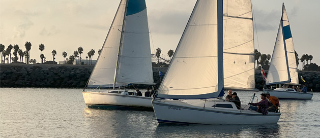 Sailboats on calm water at dusk with palm trees in the background.