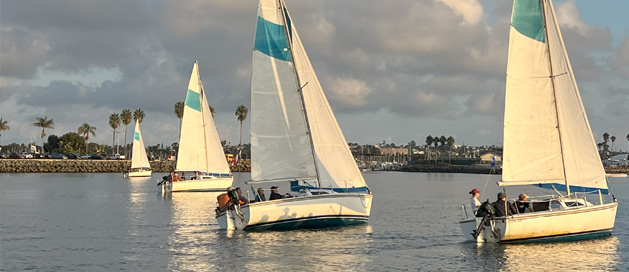 Sailboats with white and teal sails on the water at sunset.