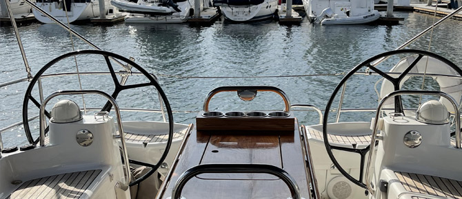 View from the stern of a boat with twin steering wheels, overlooking a marina.