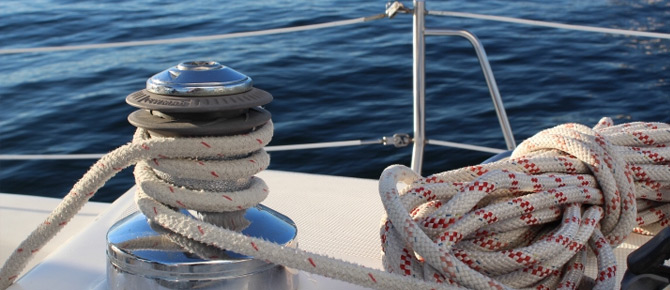 A winch with coiled rope on a sailboat deck with the ocean in the background.