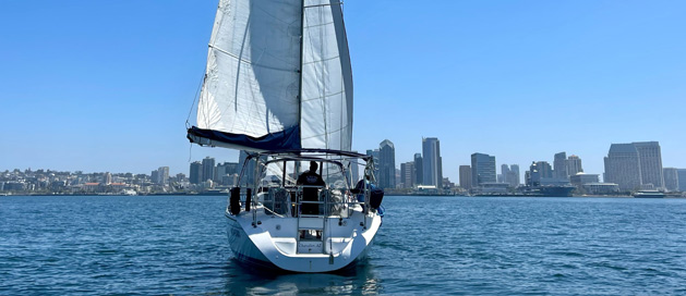 A sailboat on calm waters with a city skyline in the background.