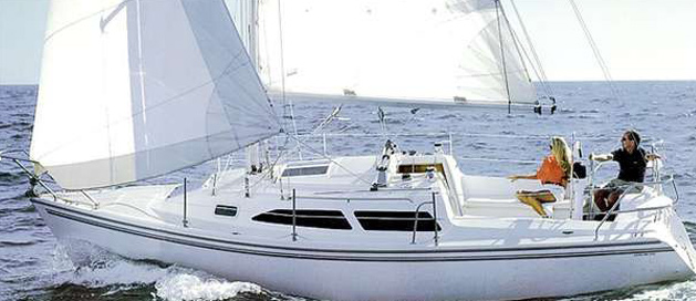 A sailboat with three people on board gliding over blue water with hills in the distance.