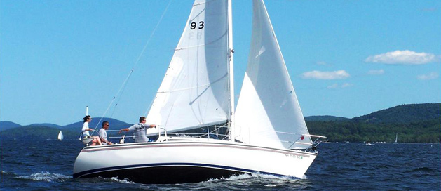 A sailboat with three people on board gliding over blue water with hills in the distance.