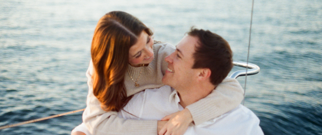 Two people embracing on a boat with the ocean in the background.
