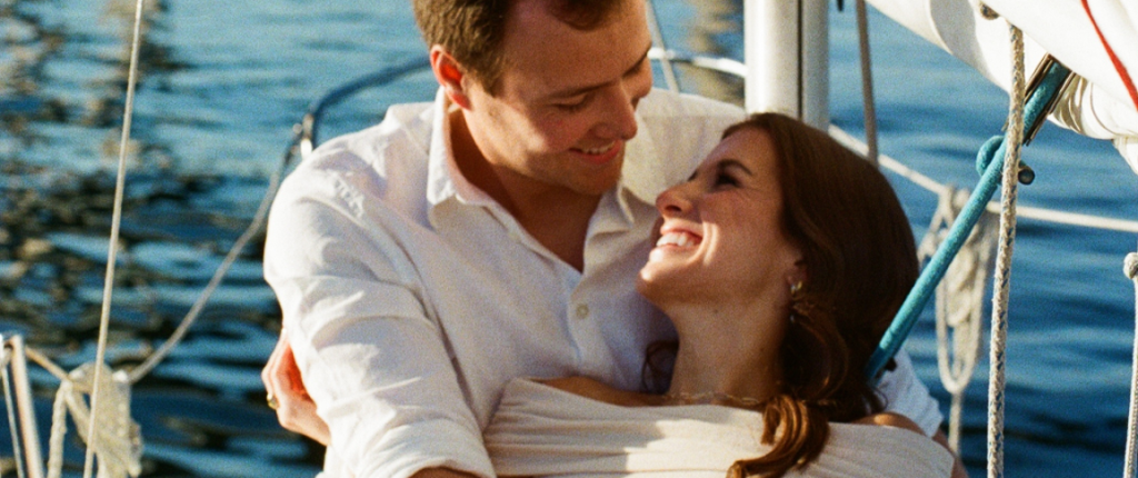 Two People Embracing On A Sailboat With The Water In The Background.