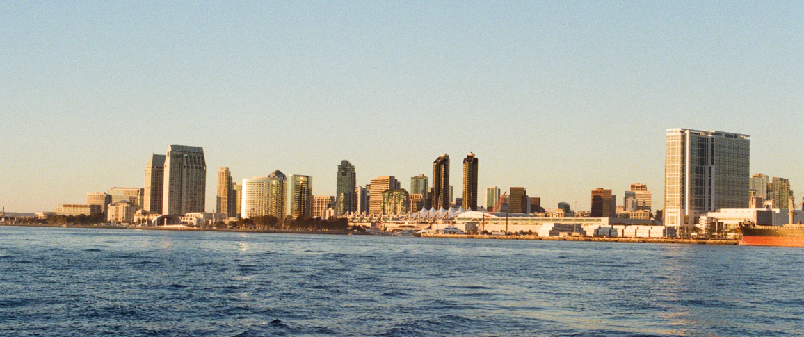 Skyline of a coastal city at sunset with reflections on the water.