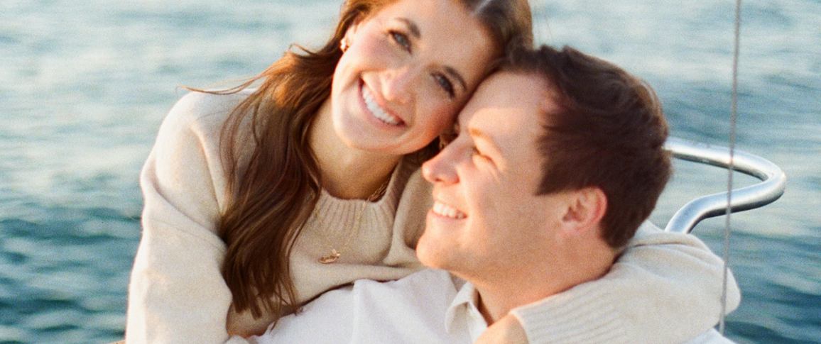 A couple embracing on a boat with a backdrop of water.