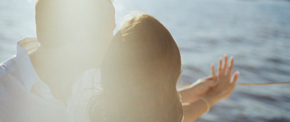 Two silhouetted figures against a bright light near water, details obscured, with a vintage feel.