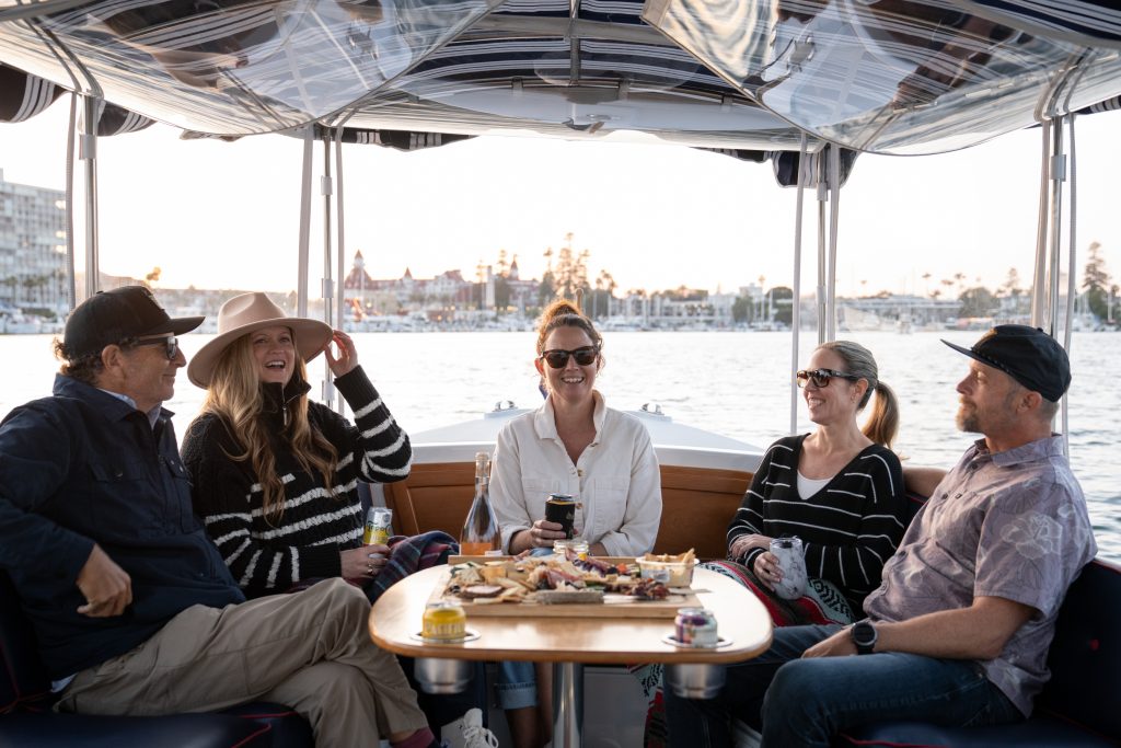 A Group Of Adults Enjoying A Boat Ride With Snacks And Drinks At Sunset.