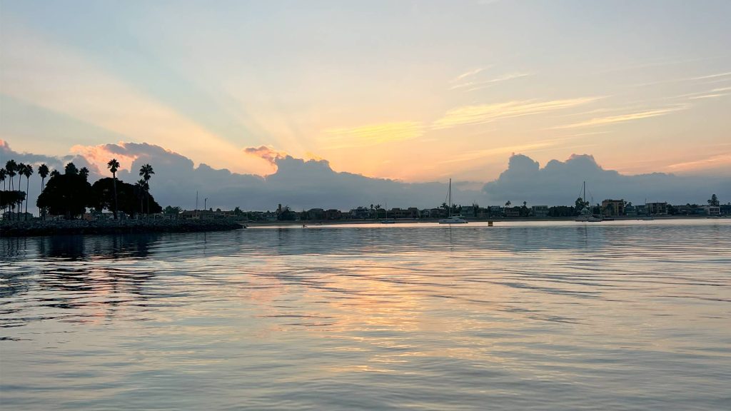 A vibrant sunset over water with clouds and boats
