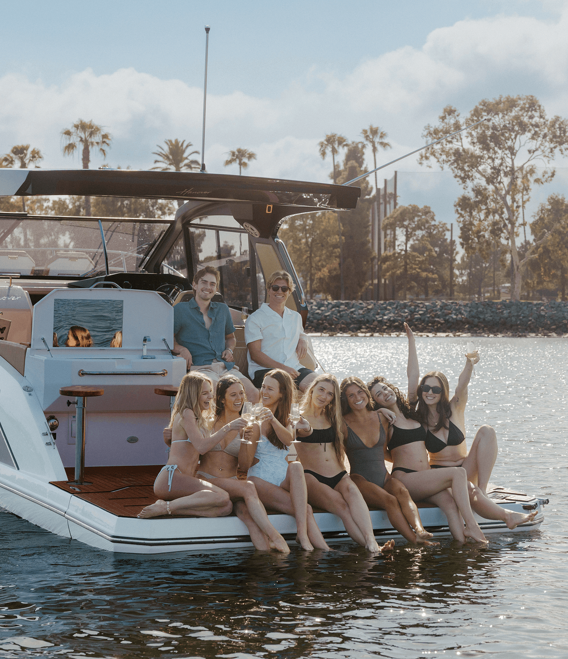 A Group Of Women In Swimsuits Enjoying Time On A Luxury Boat, Smiling And Raising
