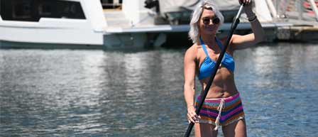 A woman in a bikini stands on a boat, paddle in hand