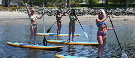 A group of women in bikinis paddle boarding on calm water at Seaforth Boat Rentals.