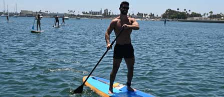 A man stands on a paddle board in calm water, enjoying a day at Seaforth Boat Rentals.