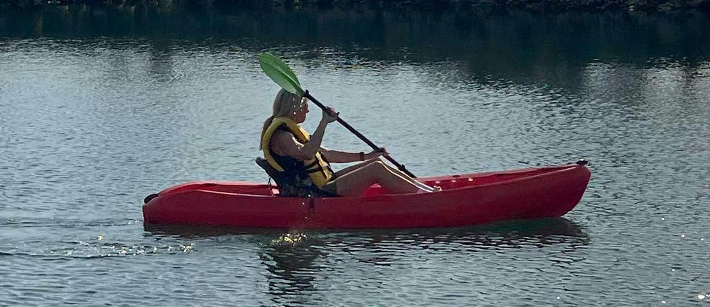 A woman in a red kayak paddles through calm water