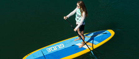 A woman stands on a paddle board in calm water, enjoying a sunny day at Seaforth Boat Rentals.