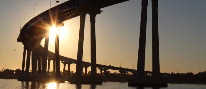 A sunset casts warm colors behind a bridge over water