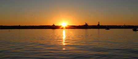 The sun sets over water with a city skyline, featuring Seaforth Boat Rentals in the foreground.