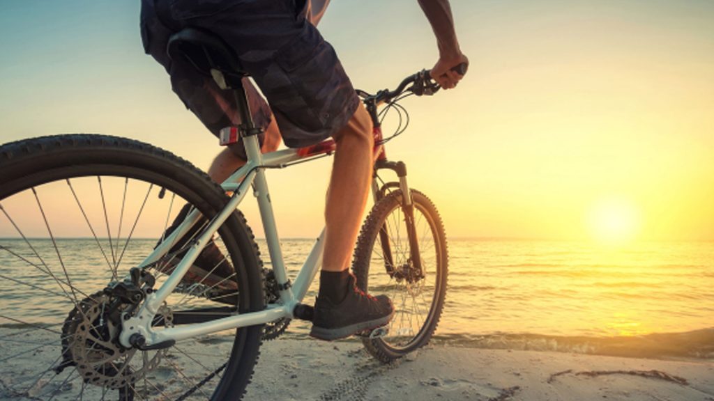 A person cycling on the beach at sunset, with Seaforth Boat Rentals in the background