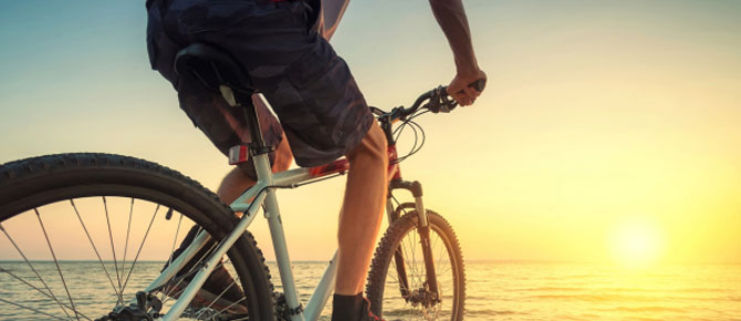 A person cycling on the beach at sunset, with Seaforth Boat Rentals in the background