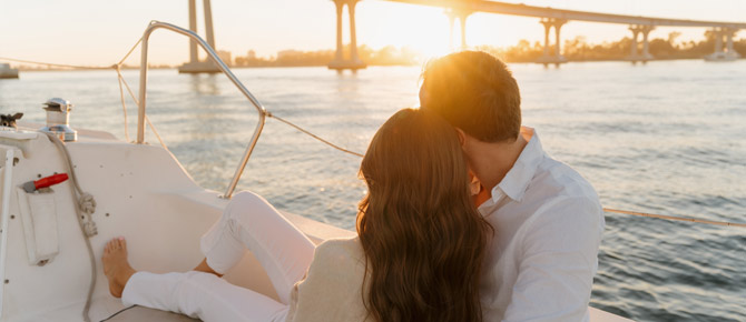 A loving couple stands together on a yacht during a sunset bay proposal, capturing the perfect engagement on the water moment.